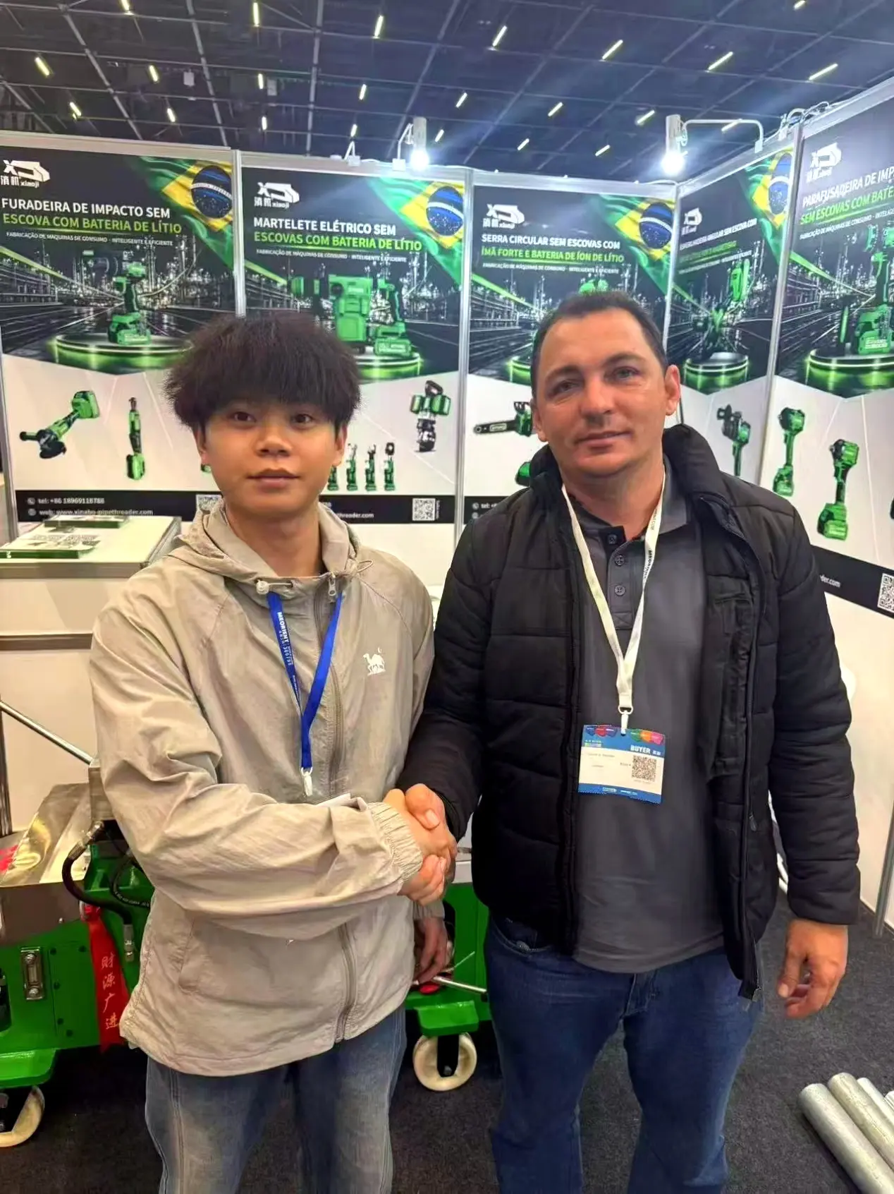A XINABO representative shaking hands with a visitor in front of cordless power tool displays